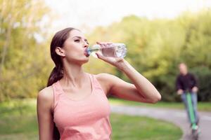 Athletic woman standing running track in summer park drink water after running exercises photo