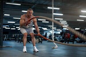 Muscular athletic bodybuilder fitness model training battle rope gym photo