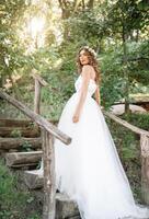 un linda Rizado mujer en un blanco Boda vestir con un Boda ramo de flores y guirnalda en su pelo en pie espalda a el cámara en naturaleza. concepto escapado novia. adelante a un contento brillante futuro huir foto