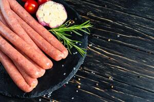 Juicy sausages for barbecue lie on a stone chopping board with rosemary and spices, pepper and coarse salt photo