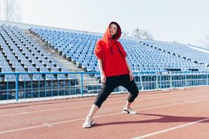 Beautiful girl in sportswear standing on the running track and preparing to run. Morning warm-up before exercise. photo