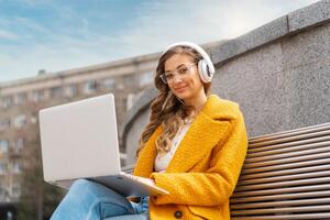 Business Woman Wear Eyeglasses Listen Music Headphone Outdoor Sitting Bench Using Laptop Outdoor photo