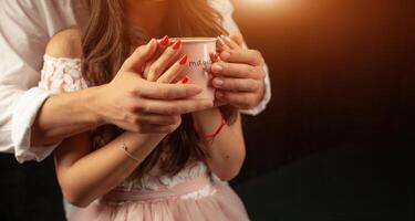 unrecognizable man and woman hold with two hands a mug of hot coffee. Couple in love. Love care concept. photo