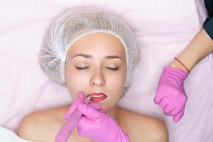 Cosmetology cabinet client lies on couch Beautician applies marking on lips. photo