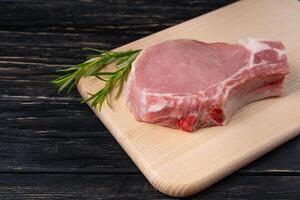 Top view of one pieces raw pork chop steaks with rosemary on a cutting board. photo