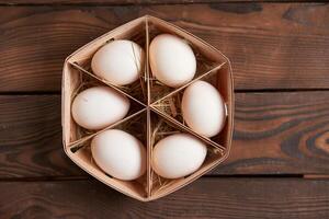 White chicken eggs lie in round wooden basket which stands on a dark wooden table. photo