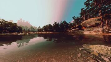 A lake surrounded by trees and rocks under a blue sky video