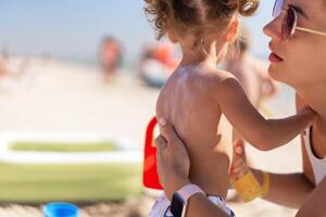 Caring mother apply sunblock to the back of her little daughter. Summer vacation sea beach photo