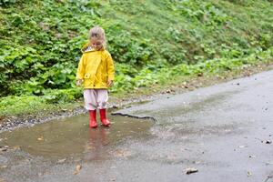 Playful girl wearing yellow raincoat while jumping in puddle during rainfall photo