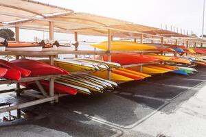 In sunlight, red, yellow and white kayaks placed upside down on metal storage racks. Stocked canoe in the Brest, France 28 May 2018 photo