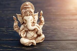 Hindu god Ganesh on black background. Statue on wooden table photo