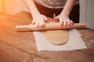 Hands rolling dough for gingerbread on the wooden table photo