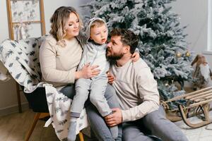 Christmas Family Happiness Portrait of dad, pregnant mom and little son  sitting armchair at home near Christmas tree hug smile photo