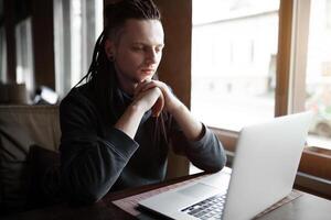 joven empresario con rastas teniendo haciendo su trabajo en café con ordenador portátil. foto