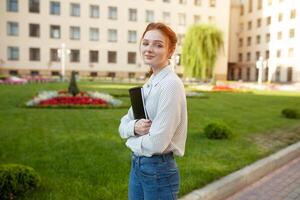 Beautiful red haired girl with freckles hugging notebooks with homework and smiling happy. Back to school concept. Portrait of a student photo