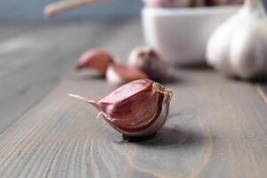 un púrpura ajo Clavo de cerca acostado cerca un plato de ajo. picante Condimento en gris antecedentes foto