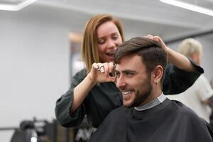 hermoso azul ojos hombre sentado en Barbero tienda. estilista peluquero mujer corte su cabello. hembra Barbero. foto