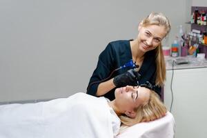 Cosmetology cabinet client lies on couch. Beautician applies marking on eyebrows. photo