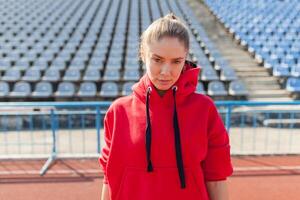 Young sports woman in sweatshirt resting after jogging training on the running track at summer photo