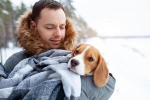 A young man wrapped his best friend Beagle dog in a warm blanket to warm him in a cold snowy winter. photo