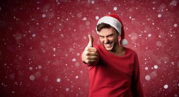 Young handsome caucasian guy in a red sweater and Santa hats stands on red background in studio and showing thumbs up. photo