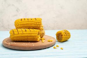 Grilled hot Corn cob lies on cutting board blue wooden table background. photo