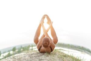 A beautiful Caucasian girl in a black swimsuit do yoga position on nature against the backdrop of the bright sun. photo