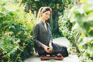 Oriental Master of tea ceremony in summer park. Traditional tea party on the nature with woman dressed in the gray shirt photo