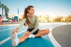 Female runner doing stretching exercises sitting on running track photo