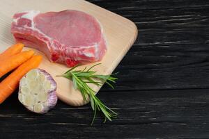 Top view of one pieces raw pork chop steaks with cherry tomatoes rosemary and garlic on a cutting board. photo