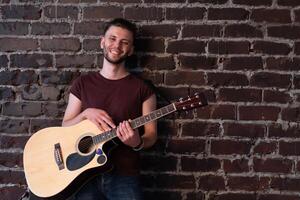 Man with acoustic guitar against brick wall playing music singing songs enjoy life Medium shoot photo