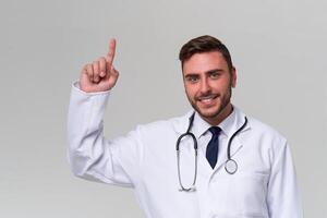 Young handsome modern doctor in a white medical gown stands in the studio on a white background. Student trainee of a medical university. photo