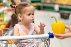 Little Caucasian girl chooses fresh vegetables in the supermarket. photo