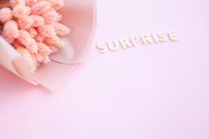 Beautiful pink dried flowers on a pink background with the inscription surprise in white letters and free space for the text photo