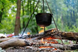 Camping outdoors. Cooking bowler hat hung on tripod over bonfire photo