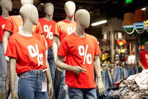 Percentage sign painted on a red t-shirt dressed on a mannequin stands in defocused store photo