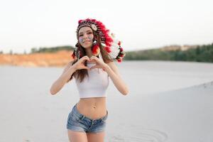 un hermosa joven caucásico niña en un blanco parte superior en su cabeza es vistiendo un indio sombrero. cucaracha es en el desierto. contento fiesta humor. foto