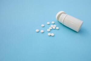 Pills and pill bottle on blue paper background photo