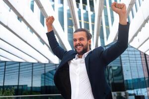 emocionado joven empresario en traje celebrando victoria brazos elevado foto