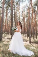 un linda Rizado mujer en un blanco Boda vestir con un Boda ramo de flores y guirnalda en su pelo en pie espalda a el cámara en naturaleza. concepto escapado novia. adelante a un contento brillante futuro huir foto