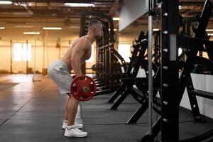 Muscular athletic bodybuilder fitness model standing in front of mirror back to camera training lift barbell indoor gym photo