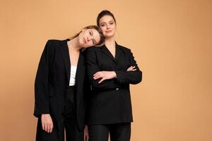 Two young business woman dressed black suit standing studio orange color background photo