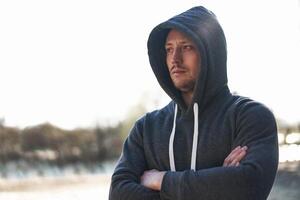 Young handsome caucasian man dark blue hoody portrait stands on the street after a jogging hood. photo