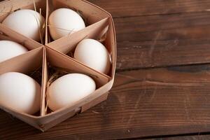 White chicken eggs lie in round wooden basket which stands on a dark wooden table. photo