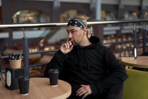 Young handsome lonely man sits cafe table sad waiting for meeting drinking coffee from a paper cup. photo