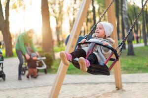 contento niño niña en columpio en puesta de sol caer. pequeño niño jugando en el otoño en el naturaleza parque foto