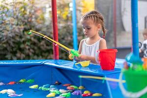 Child Fisher Catching Plastic Toy Fish On Pool Amusement Park Summer Day photo