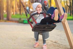Happy child girl on swing in sunset fall. Little kid playing in the autumn on the nature park photo