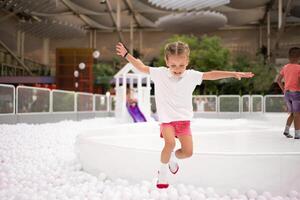 Happy little girl playing white plastic balls pool in amusement park. playground for kids. photo