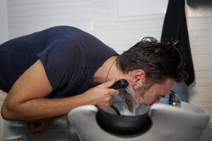 Man wash beard in beauty salon Client washing hair. Happy caucasian guy enjoy service in barbershop photo